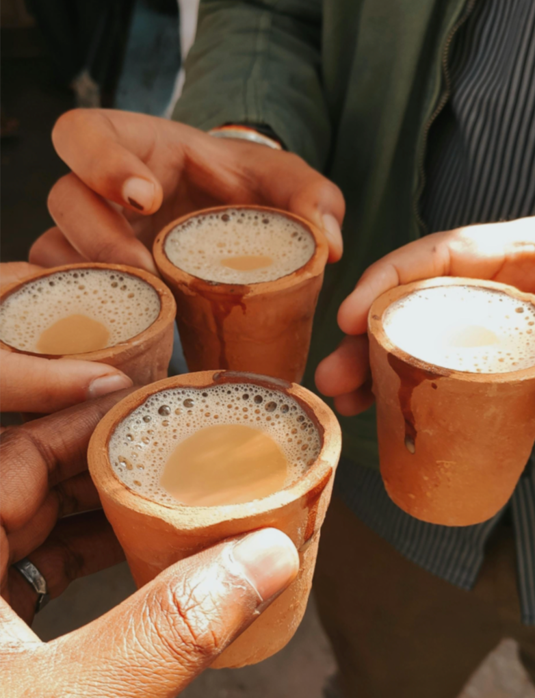 Buy authentic desi masaledar chai online – four hands holding hot masala tea in traditional kulhad cups, perfect for lovers of premium Indian masala chai.