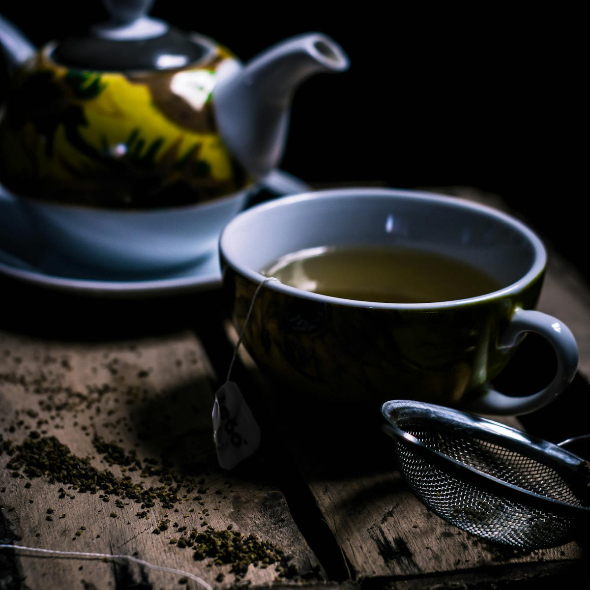 Cup of premium green tea with tea bag, fresh loose leaves, and a teapot on rustic wood – Tearaja Green Tea Collection